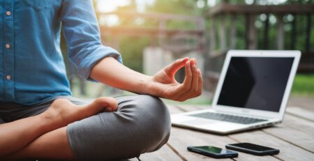 Person in lotus position meditating peacefully with smartphones and laptops in the background