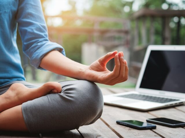 Person in lotus position meditating peacefully with smartphones and laptops in the background